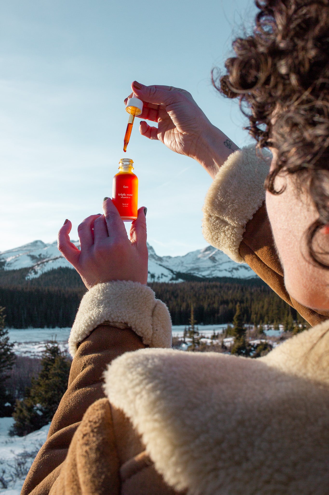 Woman gazes at glowing orange bottle of oil amidst snow-covered mountains.